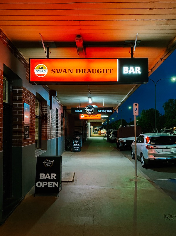 The view east along the footpath outside the Hotel at night. Customers' cars line the street.